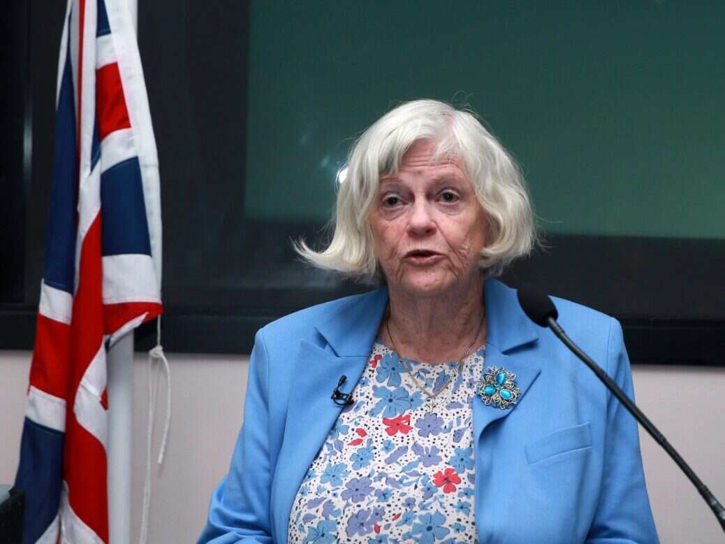 Ann Widdecombe speaking to a microphone in front of the flag of Great Britain.