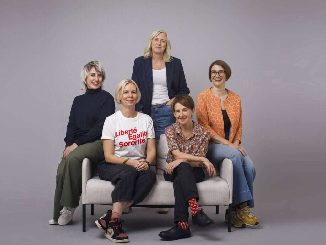 Founders of The Nerve, five women pictured sat on and standing around a sofa with a grey backdrop. Lynsey Irvine, Sarah Donaldson, Carole Cadwalladr, Jane Ferguson and Imogen Carter