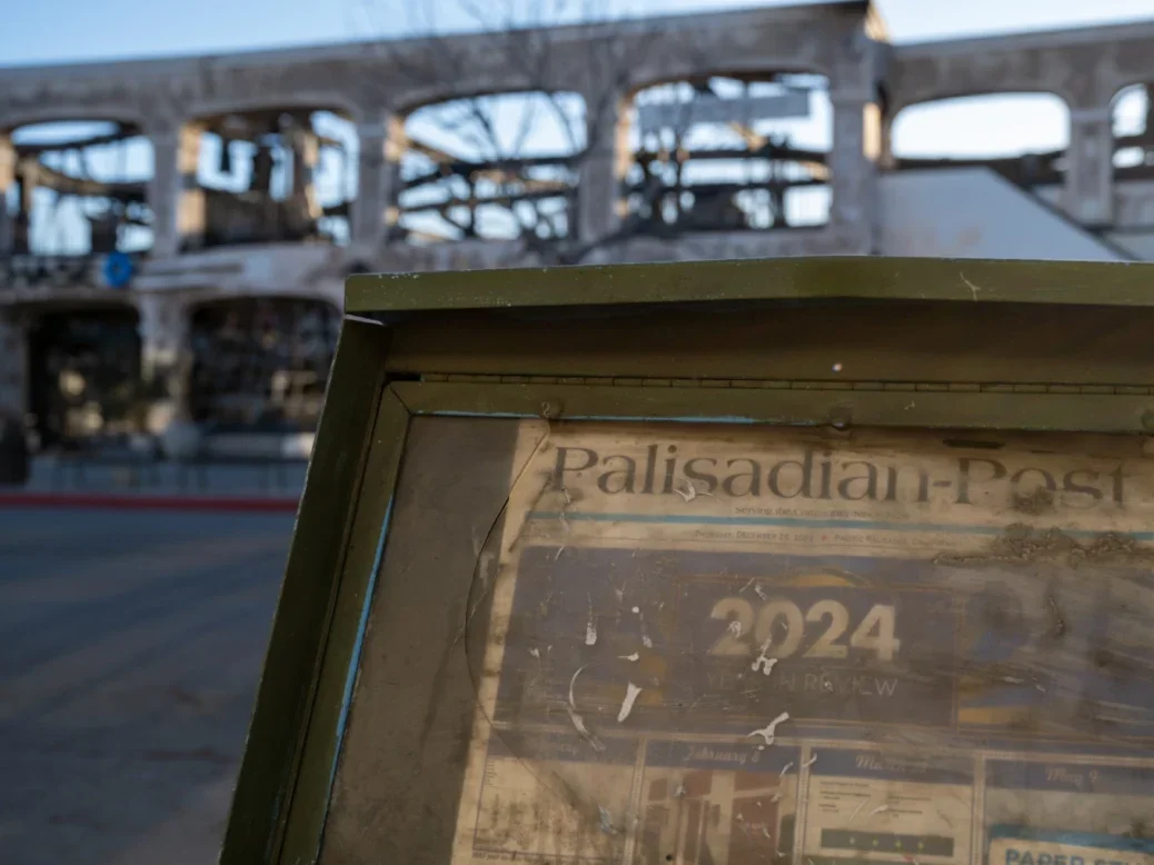 Burnt out building behind damaged newspaper distribution box showing Palisades newspaper