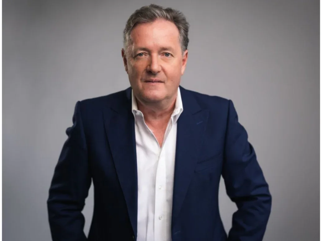 Piers Morgan in white suit, navy blazer and grey background