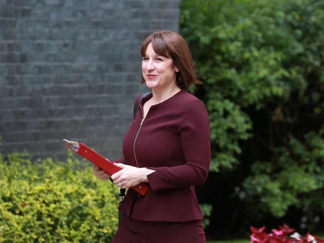 Rachel Reeves walking towards No 10 Downing Street front door holding red folder with foliage behind her and she's looking towards the camera