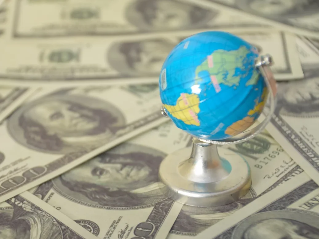 Small plastic globe placed on top of a surface covered in dollar bills
