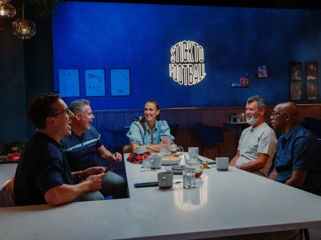 The Overlap podcast being recorded featuring four men and one woman sitting around a table with coffee mugs, mostly laughing. Sign on the wall says 'stick to football'